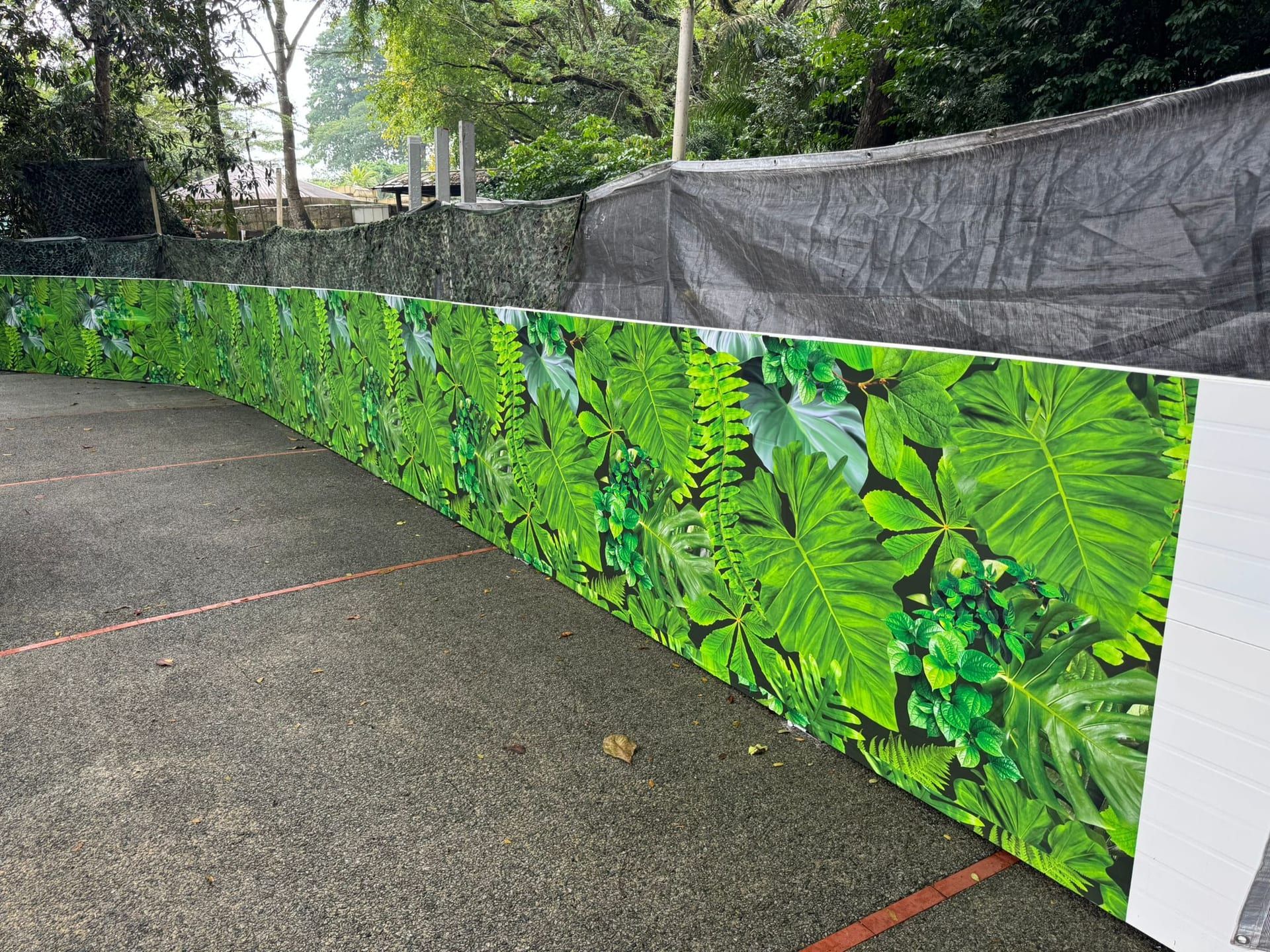 Leaf-print hoarding beside camouflage netting at a park — Hoarding Sticker Printing by Garrison Productions, Singapore